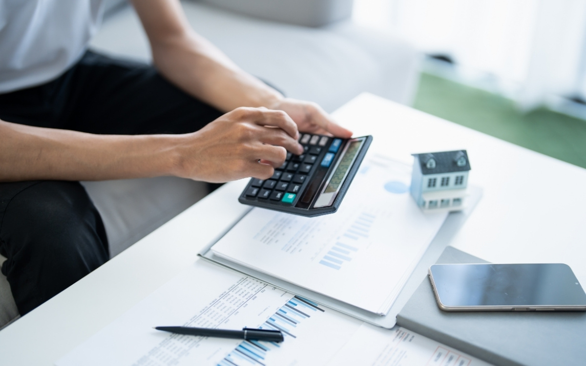 Persona calculando con una calculadora sobre documentos y gráficos junto a una maqueta de casa