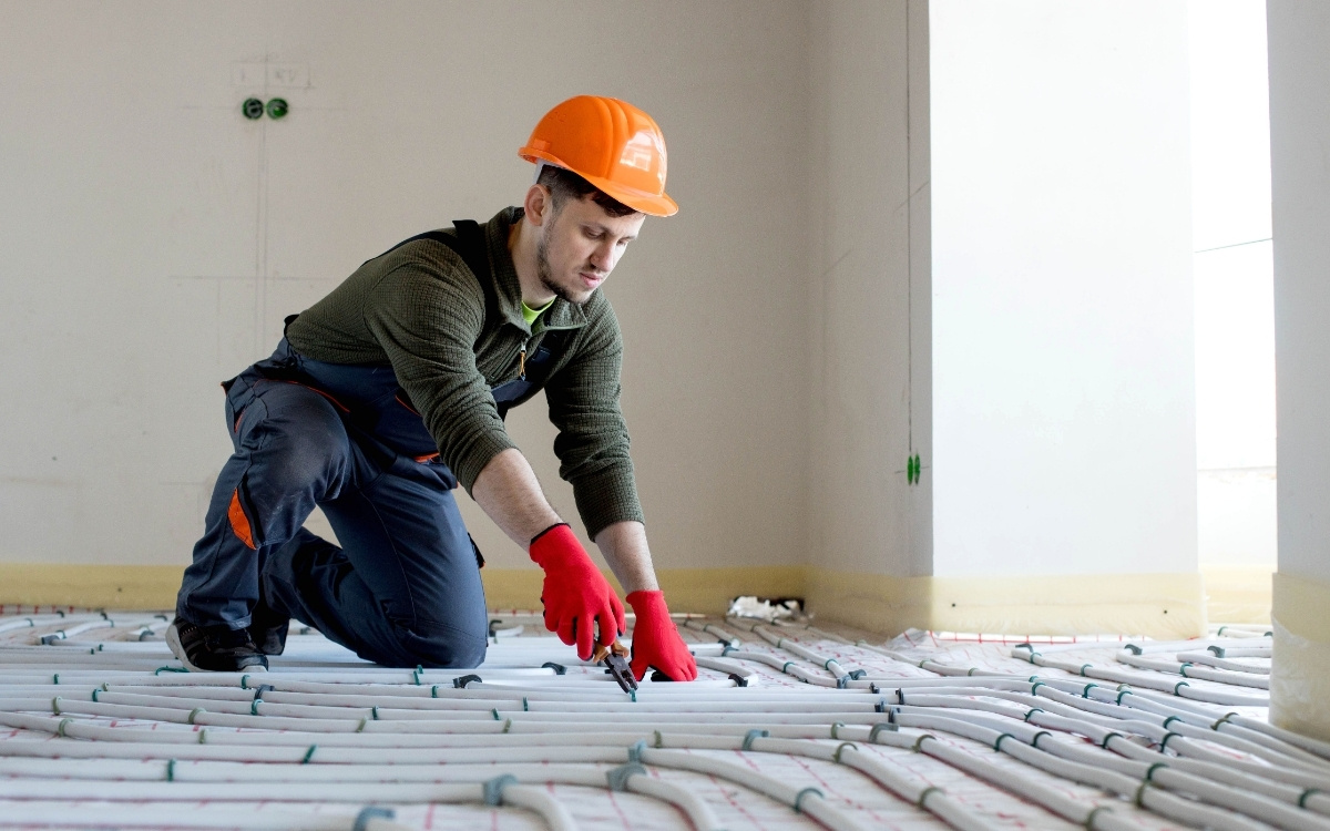 Instalador con casco naranja y guantes rojos colocando tuberías de suelo radiante en una vivienda