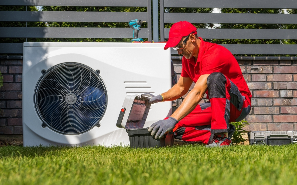 Técnico con ropa roja revisando una bomba de calor de aerotermia exterior sobre el césped